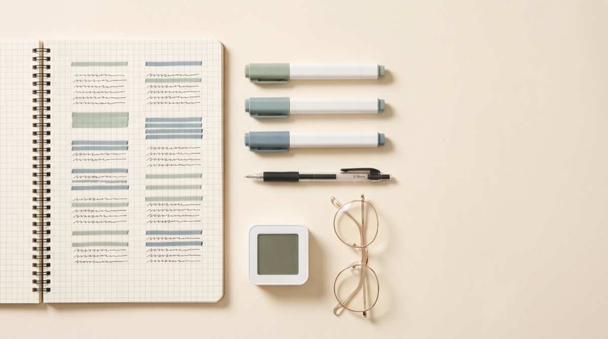 A minimal Korean-style study flat lay: an open grid-paper notebook with sage and dusty-blue highlighted blocks, three highlighters in a row, a fine gel pen, a square study timer and round wire glasses.
